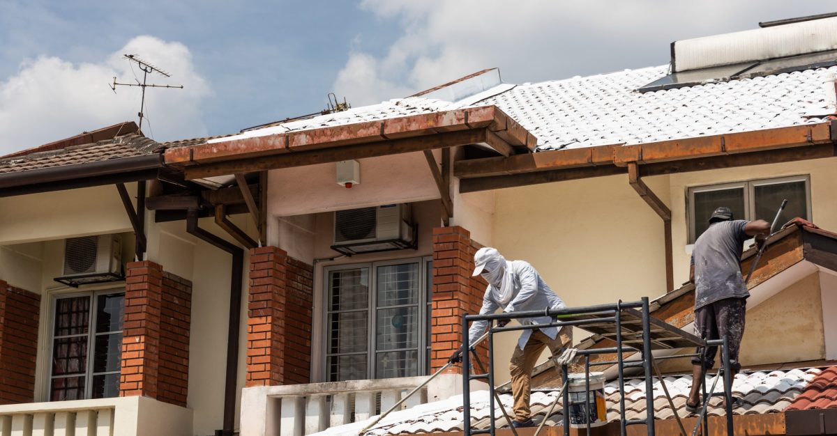Worker adding undercoat foundation paint onto rooftop with roller as primer at residential building in renovation
